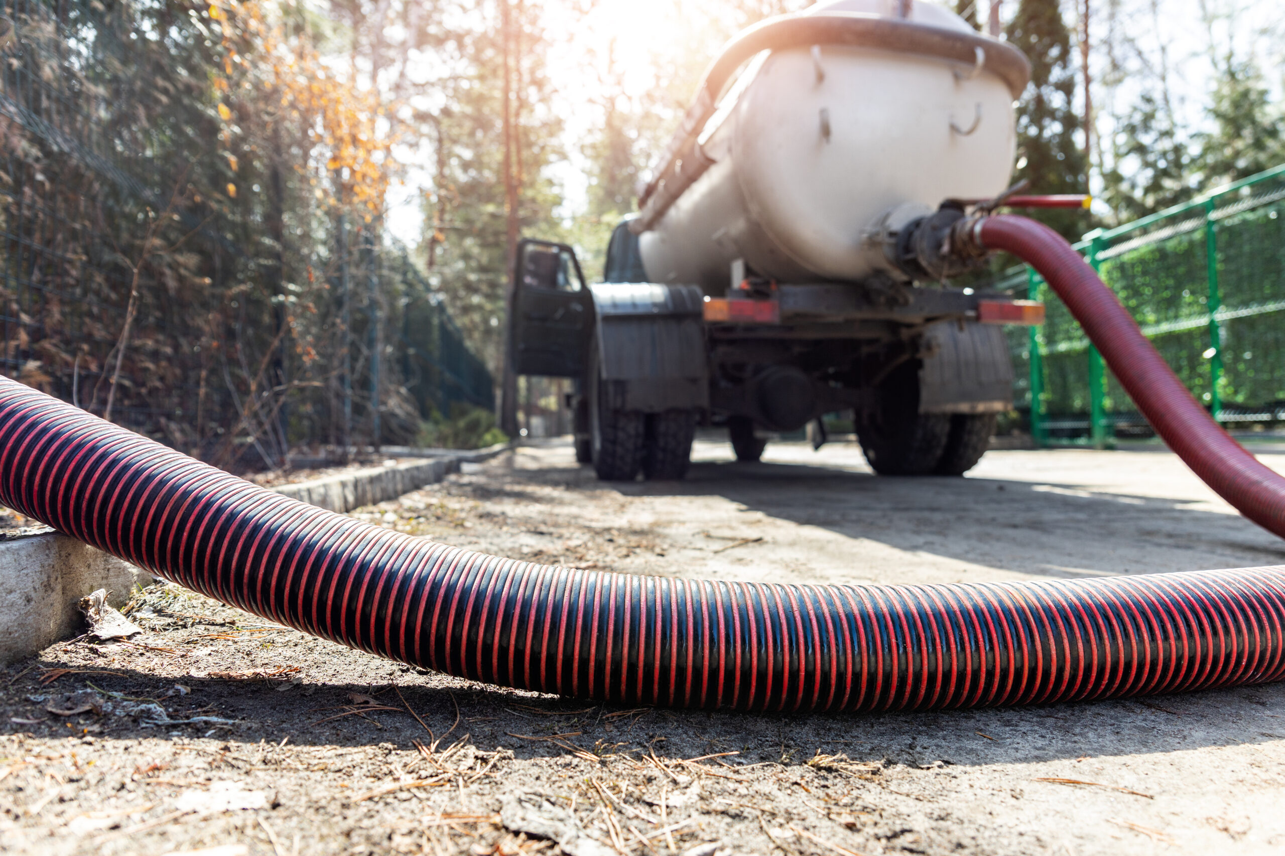 Close-up pipe hose of sewage truck car engine emptying home sewerage tank. Septic cleaning vacuum service and maintenance suburban countryside home. Suction vehicle cleaner machine pumping drainage